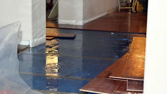Lifted hardwood floorboards over wet subfloor with plastic sheeting along the wall